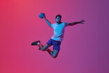 Throwing ball in jump. Young man, professional handball player training, playing isolated on gradient pink background in neon light. Concept of sport, action, motion, championship, sportive lifestyle