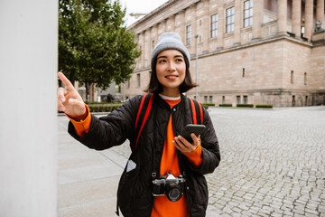 Wall Mural - Smiling asian woman tourist using smartphone during walk through the old city street