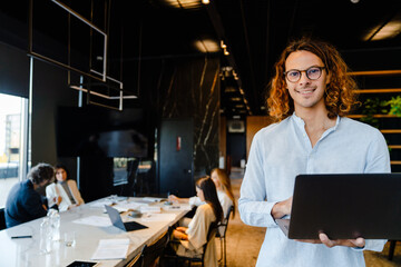 Wall Mural - Young businessman using laptop while standing in office with his colleagues on a background