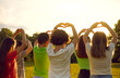 © Studio Romantic - Kids wishing for peace. Back view of group of little children standing in warm evening sunlight in green park or field, putting fingers in shape of hearts and raising hands up. Love and peace concept