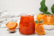 Jar of tasty persimmon jam, ingredients on white table