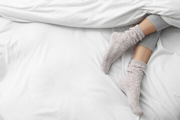 Wall Mural - Woman wearing warm socks in comfortable bed, above view. Space for text