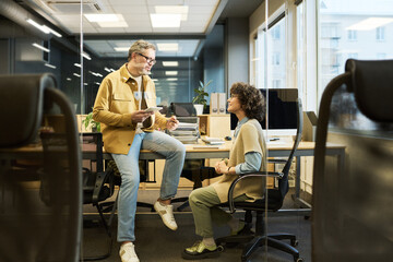 Poster - Confident mature male manager in casualwear talking to younger female colleague at meeting while using tablet with graphic data