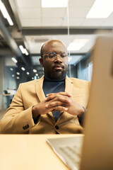 Fototapete - Young serious businessman sitting in front of laptop by his workplace in office and looking at screen while watching online video