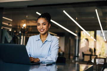 Wall Mural - Portrait of an African businesswoman sitting at the office, using a laptop.