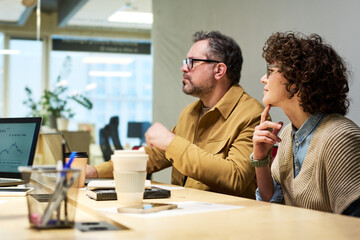 Aufkleber - Two serious colleagues sitting by desk at seminar and listening to speaker making presentation of financial data or marketing analysis