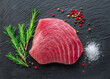 Raw tuna fish steak on natural stone black slate serving plate. Top view.