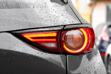 Wall Mural - Car with switched on tail light in drops of water outdoors, closeup