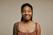 © Seventyfour - Young black woman smiling at camera standing on neutral beige background