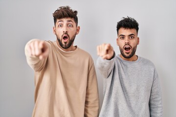 Wall Mural - Young homosexual couple standing over white background pointing with finger surprised ahead, open mouth amazed expression, something on the front