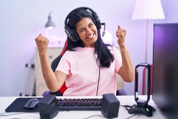 Sticker - Mature hispanic woman playing video games at home very happy and excited doing winner gesture with arms raised, smiling and screaming for success. celebration concept.