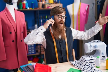 Wall Mural - Young redhead man tailor talking on smartphone with unhappy expression at clothing factory