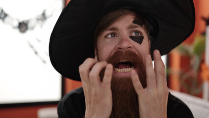 Young redhead man wearing wizard costume doing scare expression at home