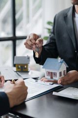 Wall Mural - Real estate agents, insurance sales agents, and young Asian businessmen handing home keys and model homes to homebuyers after signing sales contracts are satisfied in the office.