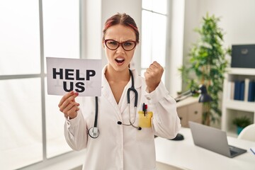 Canvas Print - Young caucasian woman wearing doctor uniform holding help us banner annoyed and frustrated shouting with anger, yelling crazy with anger and hand raised