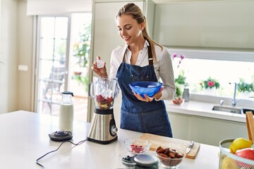 Poster - Young blonde woman smiling confident pouring ice on blender at kitchen