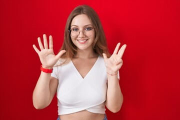 Sticker - Young caucasian woman standing over red background showing and pointing up with fingers number nine while smiling confident and happy.