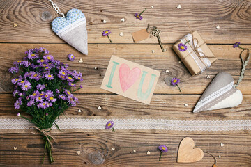 Wall Mural - Rustic greeting card background with bouquet of small purple asters, hearts and gift on old wooden boards.