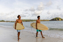 Indonesia, Lombok, Two Surfers Walking With Surfboards On Beach