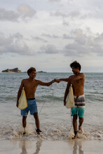 Indonesia, Lombok, Two Surfers Bumping Fists While Walking Out Of Sea
