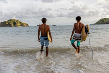 Indonesia, Lombok, Rear View Of Two Surfers Walking Into Sea