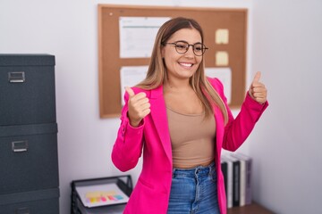 Sticker - Young blonde woman standing at the office success sign doing positive gesture with hand, thumbs up smiling and happy. cheerful expression and winner gesture.