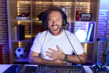 Sticker - Middle age man with beard playing video games wearing headphones smiling and laughing hard out loud because funny crazy joke with hands on body.