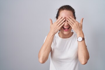 Sticker - Beautiful brunette woman standing over isolated background covering eyes with hands smiling cheerful and funny. blind concept.