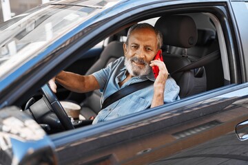 Wall Mural - senior grey-haired man talking on smartphone sitting on car at street