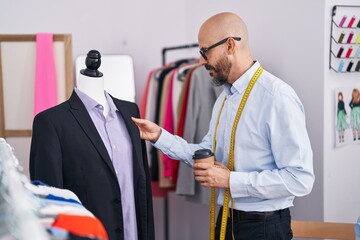 Poster - Young bald man tailor drinking coffee standing by manikin at tailor shop