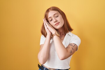 Poster - Young redhead woman standing over yellow background sleeping tired dreaming and posing with hands together while smiling with closed eyes.