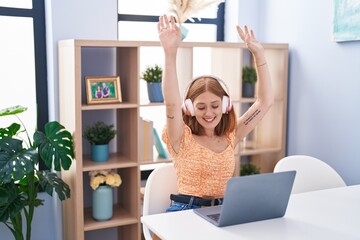 Canvas Print - Young redhead woman sitting on table listening to music and dancing at home