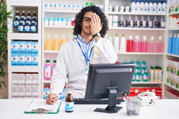 Wall Mural - Hispanic man with curly hair working at pharmacy drugstore covering one eye with hand, confident smile on face and surprise emotion.