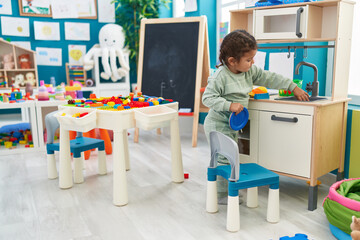 Wall Mural - Adorable hispanic toddler playing with play kitchen standing at kindergarten