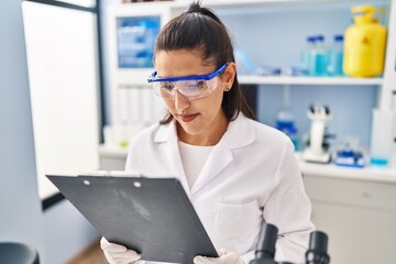 Wall Mural - Young hispanic woman wearing scientist uniform working at laboratory