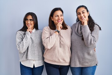 Canvas Print - Mother and two daughters standing over blue background with hand on chin thinking about question, pensive expression. smiling and thoughtful face. doubt concept.