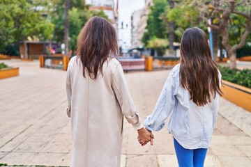 Wall Mural - Woman and girl mother and daughter walking with hands together at park