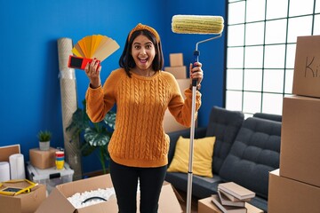 Poster - Young hispanic woman painting home walls with paint roller celebrating crazy and amazed for success with open eyes screaming excited.