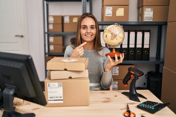 Canvas Print - Young woman working at small business ecommerce holding world ball smiling happy pointing with hand and finger