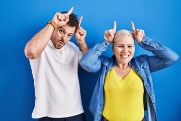 Poster - Young brazilian mother and son standing over blue background doing funny gesture with finger over head as bull horns