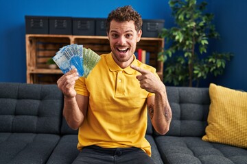 Canvas Print - Young hispanic man holding chilean pesos smiling happy pointing with hand and finger