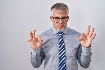 Wall Mural - Hispanic business man with grey hair wearing glasses relaxed and smiling with eyes closed doing meditation gesture with fingers. yoga concept.