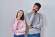 © Krakenimages.com - Young hispanic couple standing together with hand on chin thinking about question, pensive expression. smiling with thoughtful face. doubt concept.