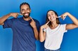 © Krakenimages.com - Young hispanic couple standing together smiling cheerful showing and pointing with fingers teeth and mouth. dental health concept.