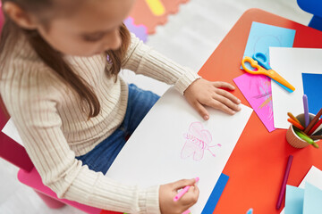 Wall Mural - Adorable hispanic girl preschool student sitting on table drawing on paper at kindergarten