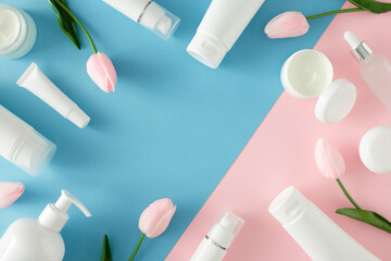 Nature skincare products concept. Flat lay photo of cosmetic tubes without label, cream jars, dropper bottles and spring flowers on  pastel pink and blue background. Organic beauty products idea.