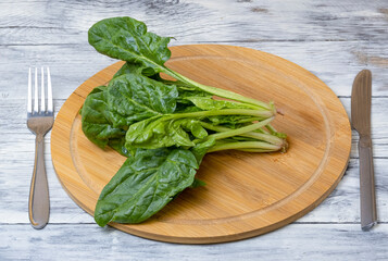 Wall Mural - Spinach leaves on a wooden plate on a wooden table. The concept of healthy food.