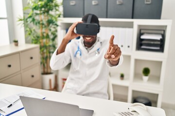 Canvas Print - Young african american man wearing doctor uniform using virtual reality glasses at clinic