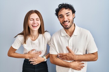 Poster - Young couple wearing casual clothes standing together smiling and laughing hard out loud because funny crazy joke with hands on body.