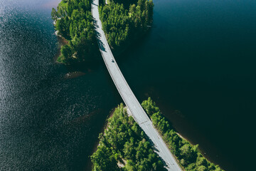 Aerial view of road over blue lake water and green woods in Finland.